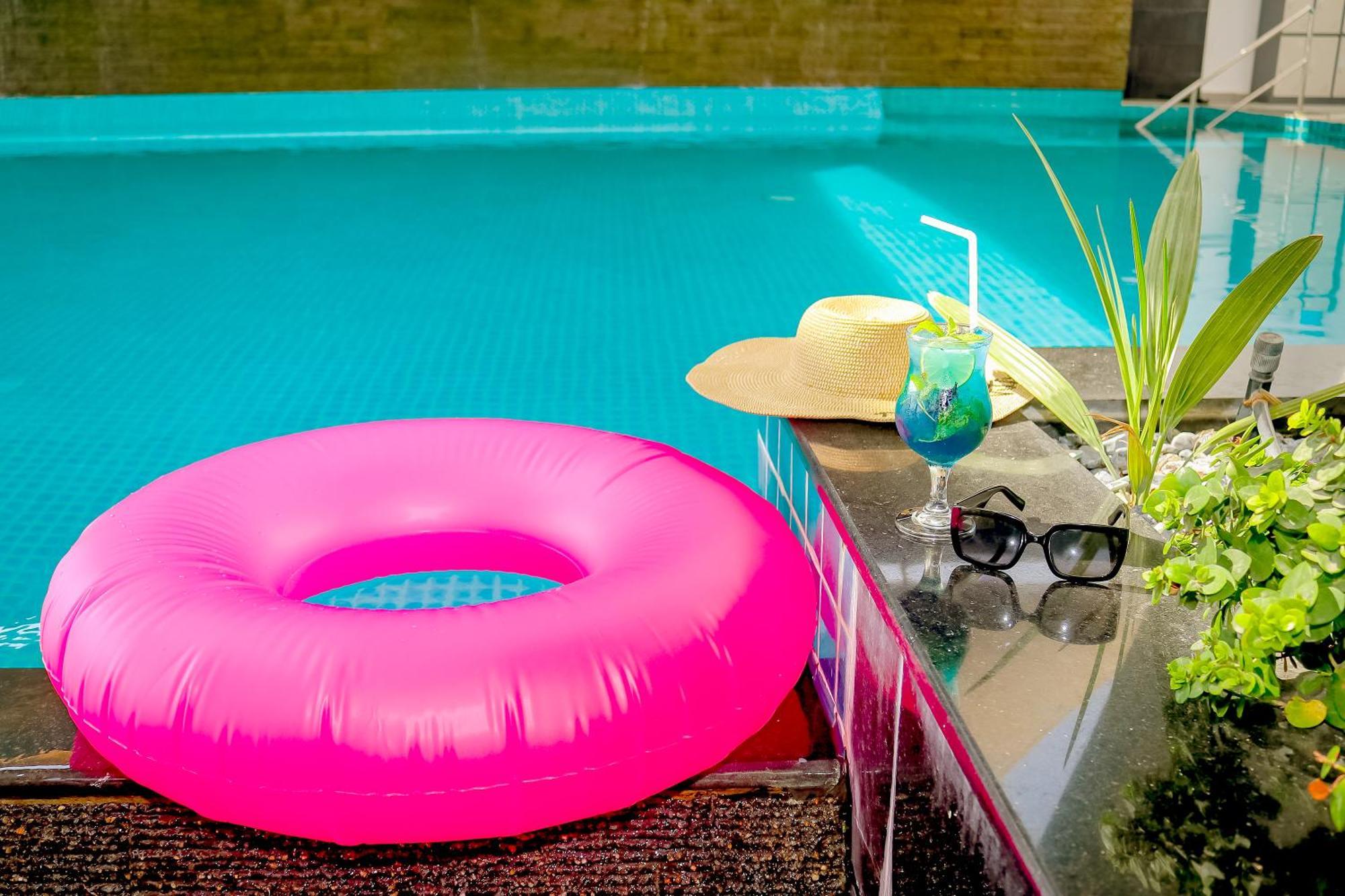 Lagoona Beach Luxury Resort And Spa Манама Екстер'єр фото The photo shows a vibrant and inviting scene by a swimming pool. In the foreground, there is a large pink inflatable float and a stylish straw hat. Next to the float, a refreshing cocktail in a glass is displayed, complete with a straw and garnishes.