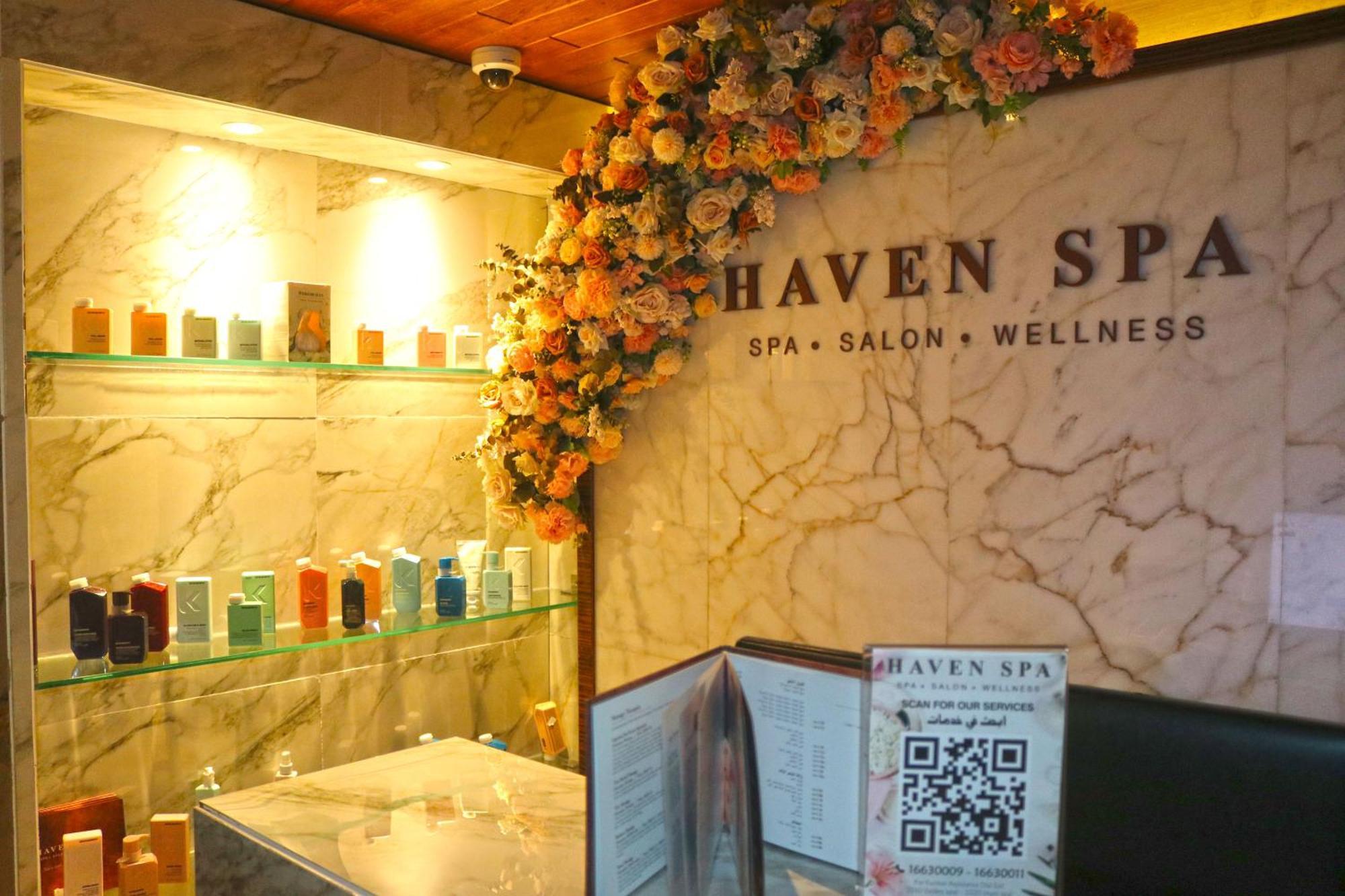 Lagoona Beach Luxury Resort And Spa Манама Екстер'єр фото The photo shows the interior of a spa called "Haven Spa." The wall is decorated with beautiful artificial flowers, creating an inviting atmosphere. There are several shelves displaying various colorful bottles and products, likely for skincare or wel