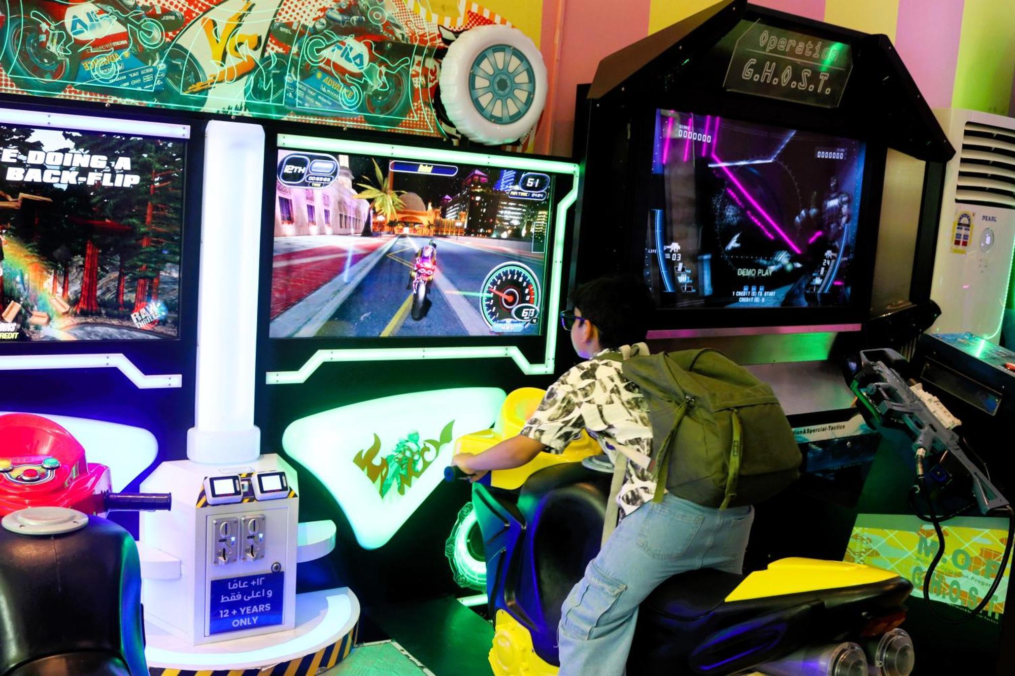 Lagoona Beach Luxury Resort And Spa Манама Екстер'єр фото The photo shows a person playing an arcade motorcycle racing game. They are seated on a motorcycle-shaped seat, actively engaging with the game displayed on the screen in front of them. The screen shows a vibrant racing scene with streets and colorfu