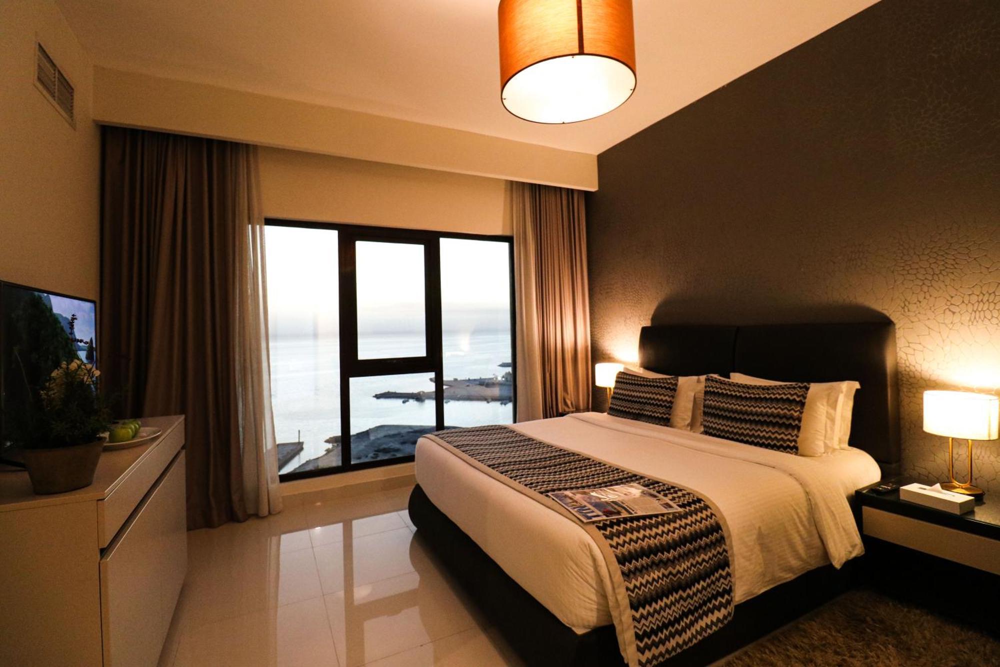 Lagoona Beach Luxury Resort And Spa Манама Екстер'єр фото The photo shows a modern hotel room featuring a neatly made bed with decorative pillows. The room has a stylish design with a dark accent wall and a large window that offers a view of the outdoors. Natural light comes in, giving the space a bright an