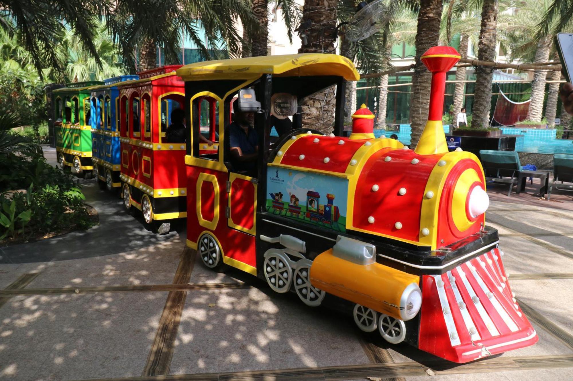 Lagoona Beach Luxury Resort And Spa Манама Екстер'єр фото The photo shows a colorful miniature train. It features a vibrant design with bright red, yellow, and blue colors. The front of the train resembles a classic steam engine, complete with a prominent smokestack. The train is designed to resemble a fun 