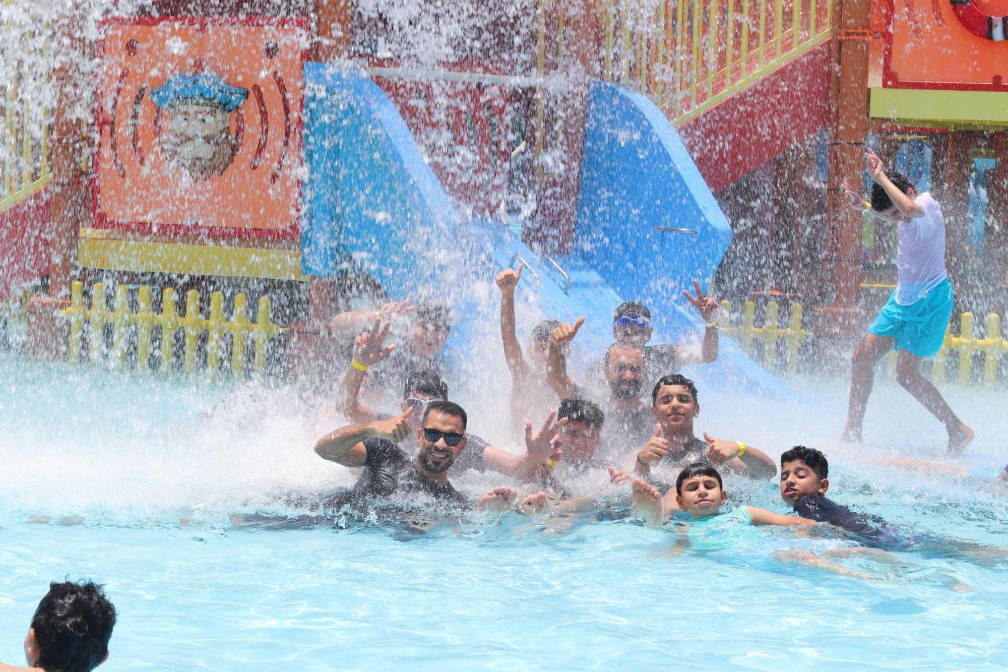 Lagoona Beach Luxury Resort And Spa Манама Екстер'єр фото The photo shows a lively scene at a water park or pool area. Several people, including adults and children, are enjoying themselves in the water, splashing and posing for the camera. Water is cascading down, creating a refreshing atmosphere. In the b