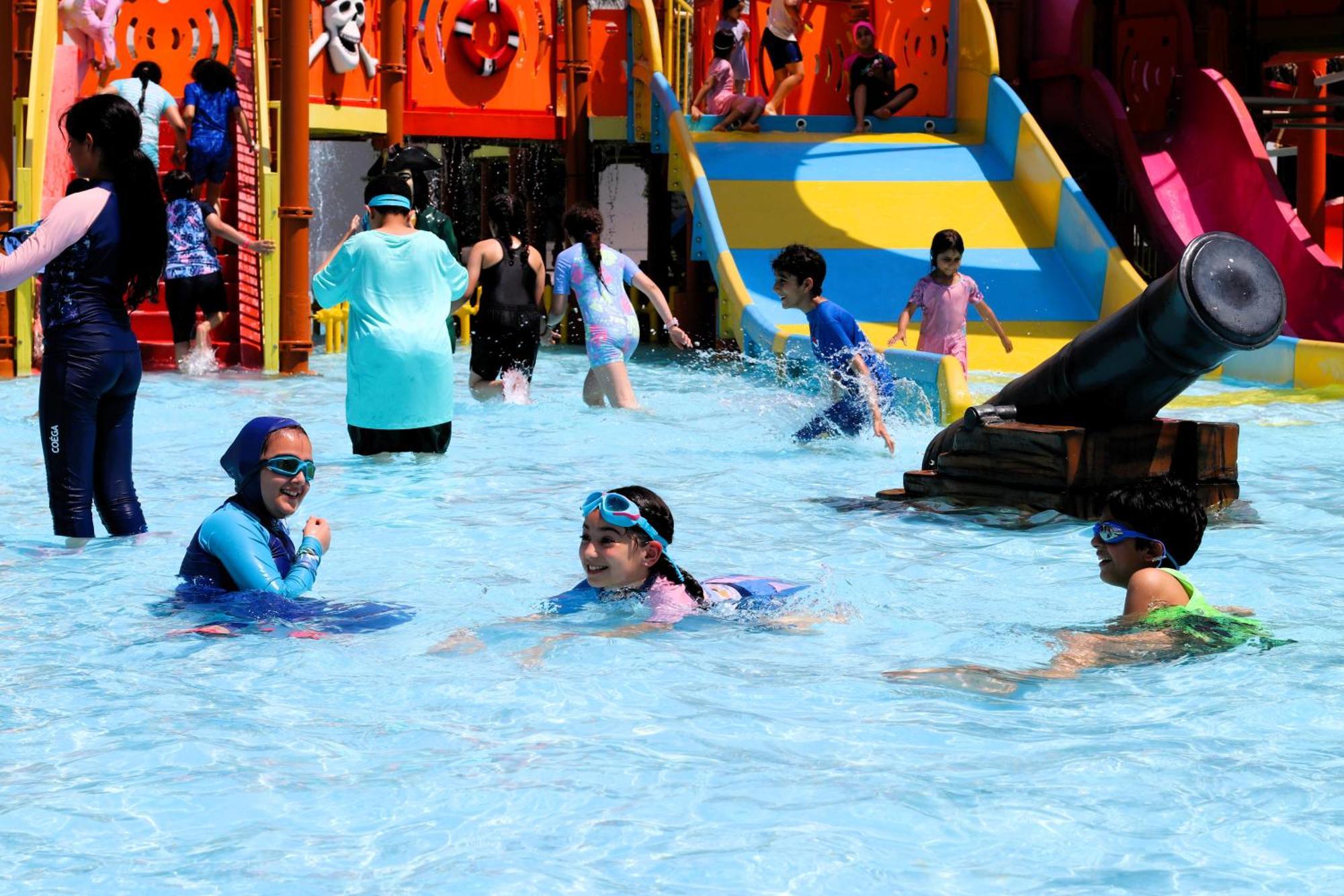 Lagoona Beach Luxury Resort And Spa Манама Екстер'єр фото The photo shows a vibrant water park scene with several children playing in a shallow pool. Some are swimming and splashing around, while others are playing on colorful slides in the background. The atmosphere is lively and cheerful, with kids of var