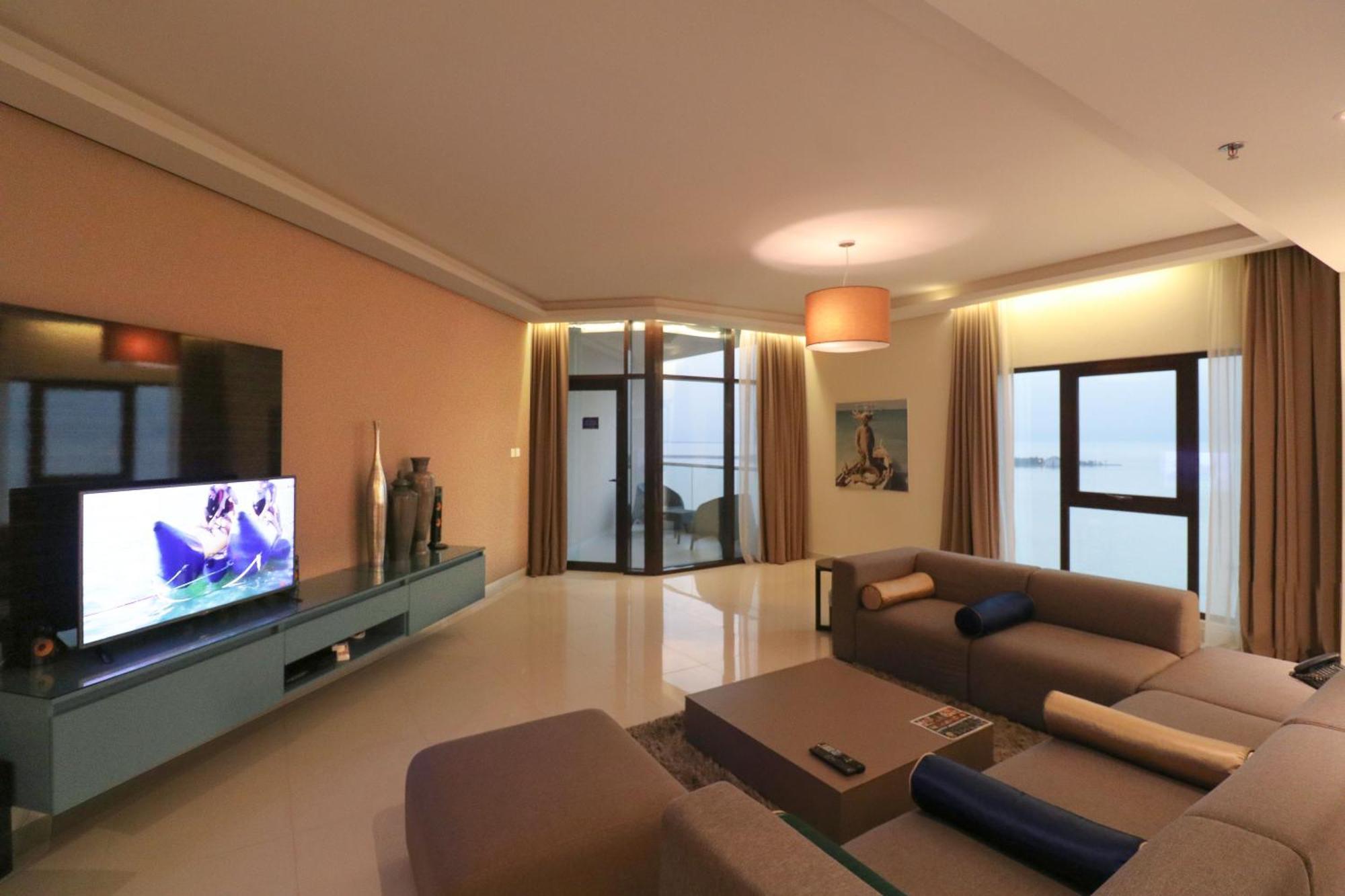 Lagoona Beach Luxury Resort And Spa Манама Екстер'єр фото The photo shows a modern living room with a sleek design. There is a large wall-mounted television on a contemporary entertainment unit, with decorative items placed beside it. The room features a comfortable sectional sofa in light tones, with a cof