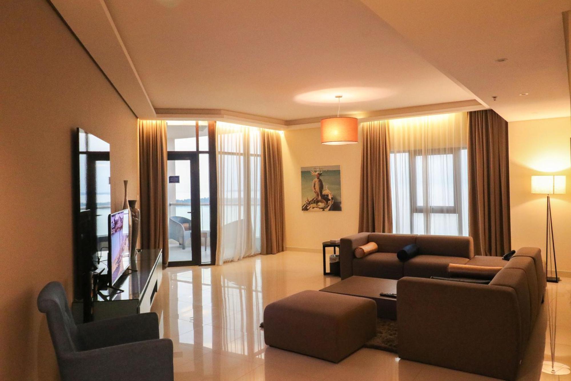 Lagoona Beach Luxury Resort And Spa Манама Екстер'єр фото The photo shows a modern living room with a spacious and elegant design. It features a large couch in neutral tones, a soft ottoman, and a stylish coffee table. The walls are painted in a light color, and there are large windows with sheer curtains a