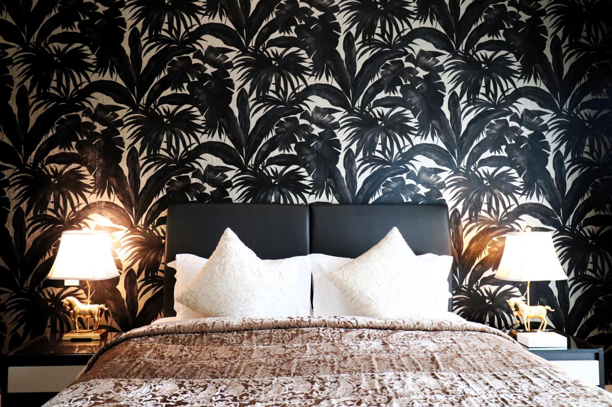 Lagoona Beach Luxury Resort And Spa Манама Екстер'єр фото The photo depicts a stylish bedroom featuring a distinctive wall covered in a black and white tropical foliage wallpaper. The bed has a modern black headboard and is adorned with white pillows, creating a clean and elegant look. A textured brown thro